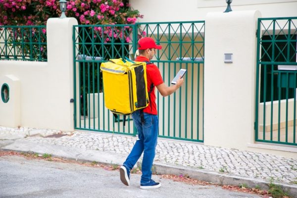 courier-with-isothermal-food-backpack-consulting-tablet-checking-address-walking-gate-doorbell-communication-delivery-service-concept_74855-11655